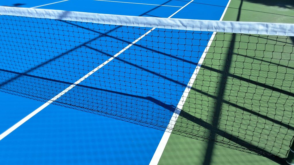 Close-up view of a tennis court with blue and green surfaces, featuring the net and shadows.